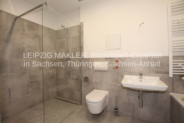 Badezimmer mit bodenebener Dusche hinter Glaswand, Toilette, Waschbecken, Fliesenwände in Grau