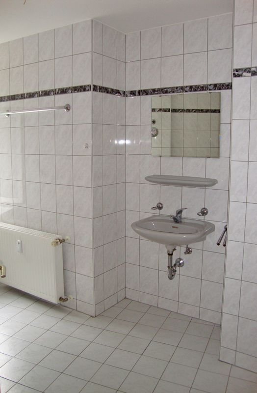 Badezimmer mit hellen Keramikfliesen, zwei Waschbecken, großem Spiegel und ebenerdiger Dusche mit Glastür