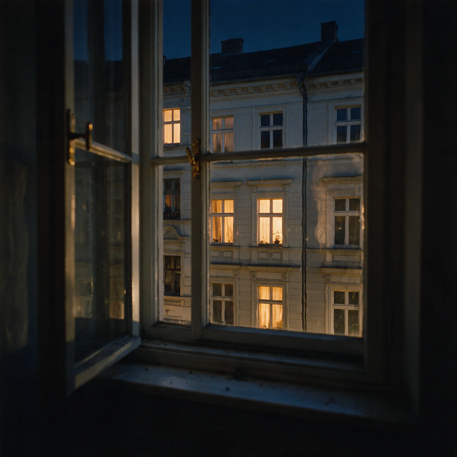 Blick aus dem Fenster einer leeren Altbauwohnung auf die Gründerzeit-Fassaden gegenüber zur blauen Stunde